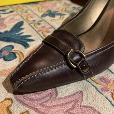 These Gorgeous Joan & David Dark Brown Leather Pumps Have Exquisite Contrast Stitching And A Fun Buckle Detail On The Toe- It Hints At A Sensible Loafer But The Eye Follows The Stitching To The Sexy Curvy Heel. They Have J&D Circa365 Technology Inside So They Are Beautiful And Comfortable! With A Glint Of Woodtone At The Heel- They’ll Look Great With A Sexy Dress For A Night On The Town Or With Jeans For Fall... Never Worn! Genuine Leather 3 Inch Heel Made In Italy For An American-Owned Company Classic Leather Court Shoes With Buckle Closure, Leather Court Shoes With Buckle For Office, Leather Court Shoes With Buckle Closure For Office, Formal Brown Faux Leather Heels, Chic Brown Leather Court Shoes, Elegant Leather Court Shoes With Buckle Closure, Formal Leather Heels With Buckle Closure, Brown Court Shoes For Formal Spring Occasions, Spring Leather Court Shoes With Heel Tab