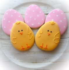 three decorated cookies sitting on top of a white plate next to pink and yellow eggs