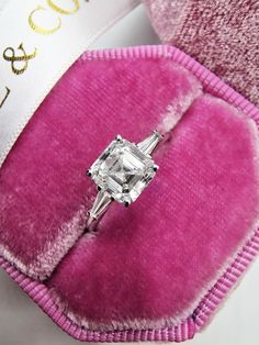 an engagement ring sits on top of a pink velvet case with a white ribbon around it