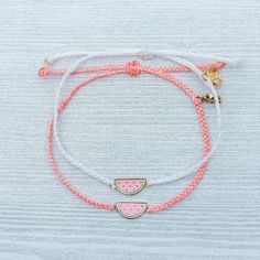 two bracelets with watermelon slices on white string and gold charms, one in the shape of a slice