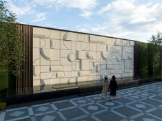 two people walking in front of a building with large letters on it's side