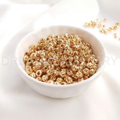 a white bowl filled with lots of gold colored beads on top of a white table