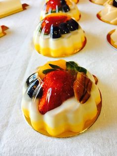 small desserts with fruit on them are lined up on a white tablecloth covered table