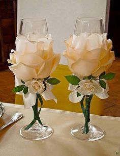 two wine glasses with flowers in them sitting on top of a table next to each other