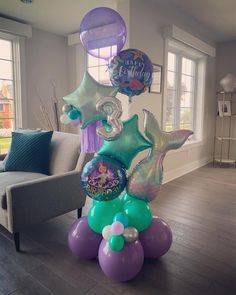 an inflatable mermaid balloon tower with balloons and other decorations on the floor next to a couch