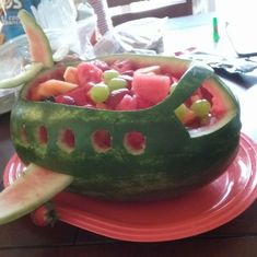 a watermelon boat filled with fruit on top of a red plate