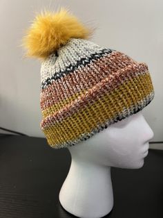 a white mannequin head wearing a multicolored hat with a yellow pom - pom