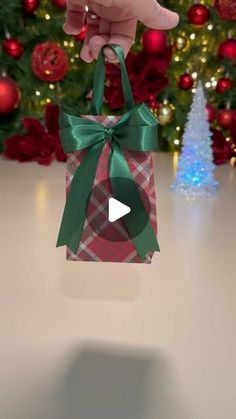 someone is holding a small gift bag in front of a christmas tree with red and green ornaments