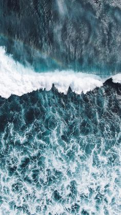 an aerial view of the ocean waves with a rainbow in the sky above it, taken from above