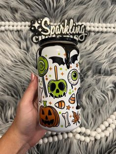 a hand holding a halloween themed tumbler on top of a fuzzy carpeted surface