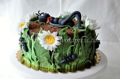 a cake decorated with grass, flowers and bugs