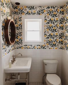 a white toilet sitting next to a sink in a bathroom under a window with yellow flowers on it