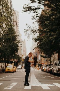 a bride and groom standing in the middle of an empty city street with taxi cabs