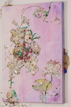 a painting on a wall with flowers and beads hanging from the side, in front of a pink background