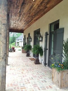 the porch is lined with potted plants and wooden posts, along with brick pavers flooring