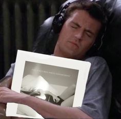 a man with headphones laying in bed while holding up a framed photo that reads the truth is unknown