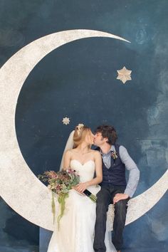 a bride and groom kissing in front of the moon painted on the wall behind them