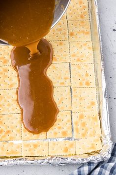 a person pouring caramel sauce on crackers in a baking pan with a blue and white checkered napkin