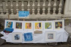 an art display with pictures and paintings on the table outside in front of a building