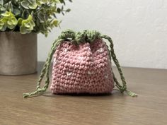 a pink crocheted bag sitting on top of a wooden table next to a potted plant