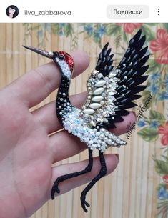 a hand holding a small bird made out of beads and pearls on it's body