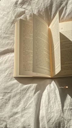 an open book sitting on top of a bed next to a white sheet covered floor