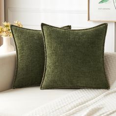 two green pillows sitting on top of a white couch next to a vase with flowers