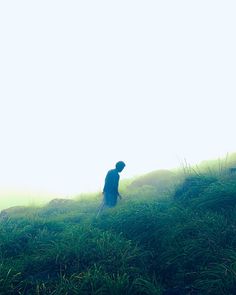 a man standing on top of a lush green hillside next to a sheep in the fog