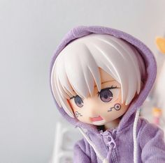 a doll with white hair wearing a purple hoodie and looking off to the side