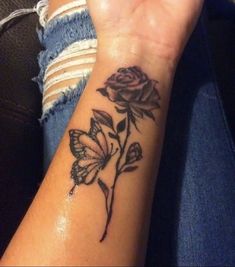 a woman's arm with a rose and butterfly tattoo on it, while she is holding her hand up to the camera