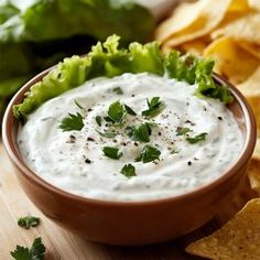 a bowl filled with white dip surrounded by tortilla chips and lettuce