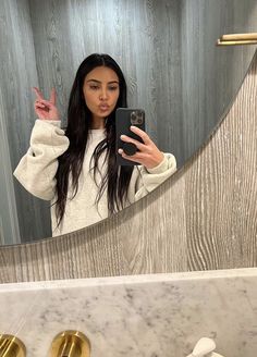 a woman taking a selfie in front of a bathroom mirror with gold faucets