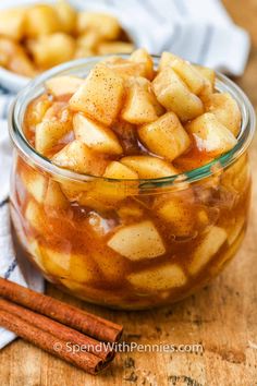 a glass jar filled with apple slices and cinnamon sticks on top of a wooden table