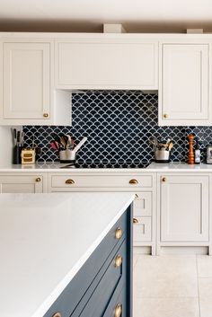 a kitchen with white cabinets and blue backsplash tiles on the countertop, along with gold pulls