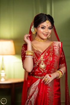 a woman in a red and gold bridal outfit posing for the camera with her hands on her head