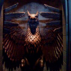 a statue of an owl with its wings spread out in front of a dark background