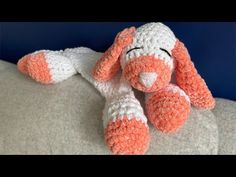 an orange and white crocheted stuffed animal laying on a bed with its eyes closed