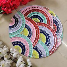 four circular placemats with colorful designs on them next to red and white flowers