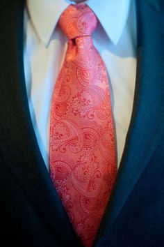 a man wearing a suit and tie with an orange paisley design on the necktie