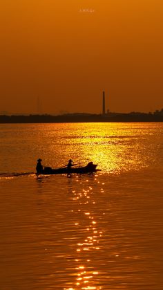 two people in a small boat on the water at sunset with an airplane flying overhead