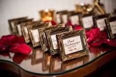 there are many small gold frames on the table with red flowers in front of them