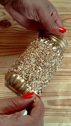 a woman is holding a gold can with red nails on her finger and it's lid open