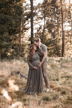 a pregnant couple cuddles in the woods for an outdoor photo session at sunset