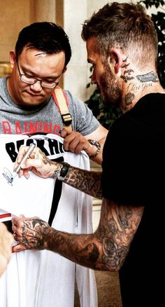 two men standing next to each other with tattoos on their arms and hands, one holding a t - shirt