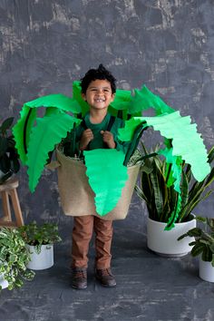 a young boy standing in front of some potted plants and holding a green plant