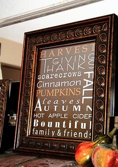 two framed pictures sitting on top of a wooden table next to apples and pumpkins