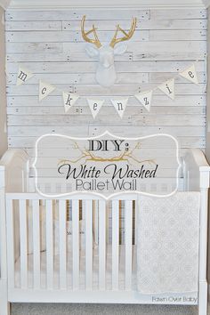 a white crib with a deer head on the wall and pennants above it