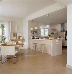 a large open kitchen and dining room with white walls, beige flooring and counter tops