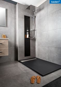 a bathroom with grey walls and flooring has a shower head, mirror, and towel rack