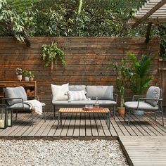 a wooden deck with chairs and couches next to a wall covered in greenery